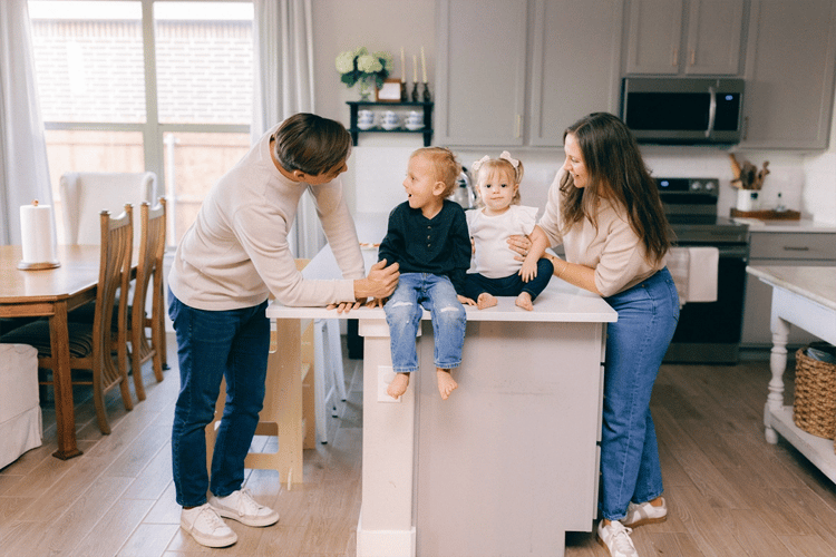 Photo of a husband and wife interacting with their young son and daughter who are sitting on the kitchen peninsula in their Betenbough home.