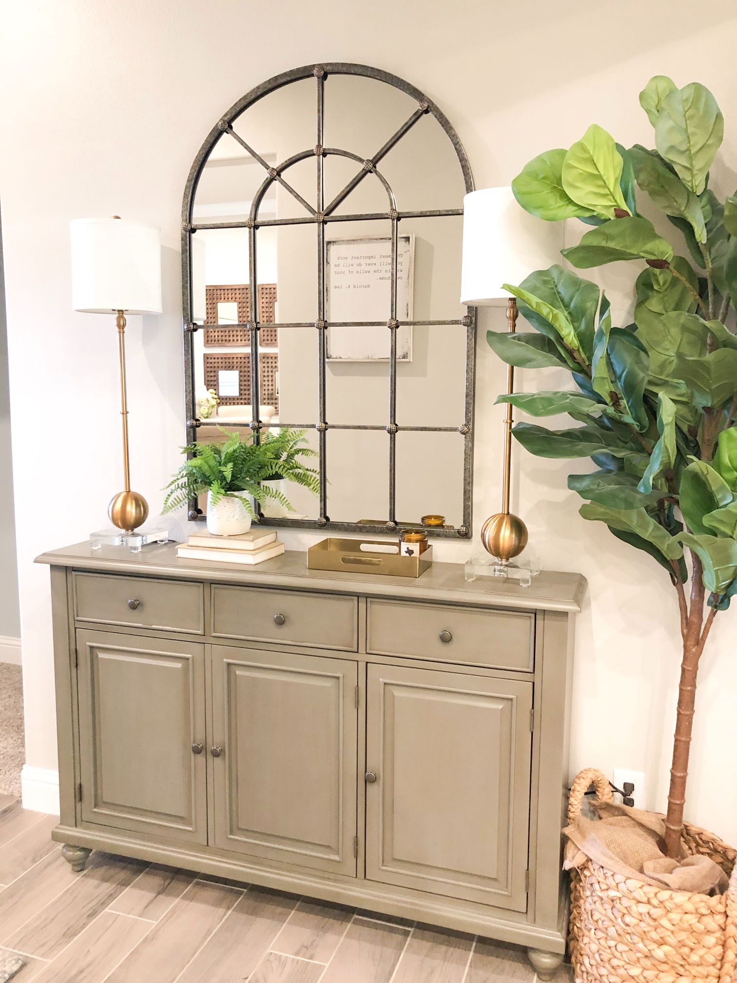 Photo of an entryway with a cabinet, mirror, lamps, plus a plant and a potted tree for touches of green.