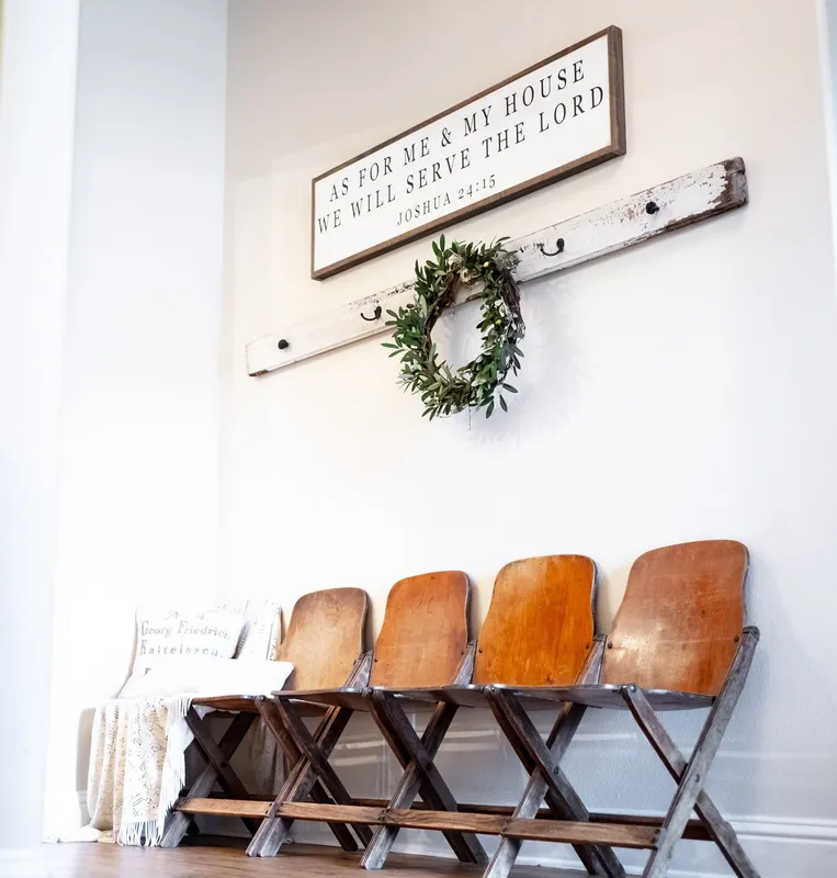 Photo of a home's decorated entryway with coat hooks, a scripture sign, antique seating, and a blanket and pillows.