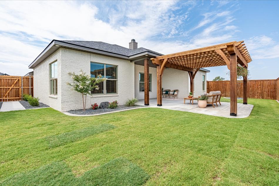 Photo of a lush, green Betenbough home backyard with landscaping, a cedar pergola, and patio furniture -- a dream-come-true for any first-time home buyer.