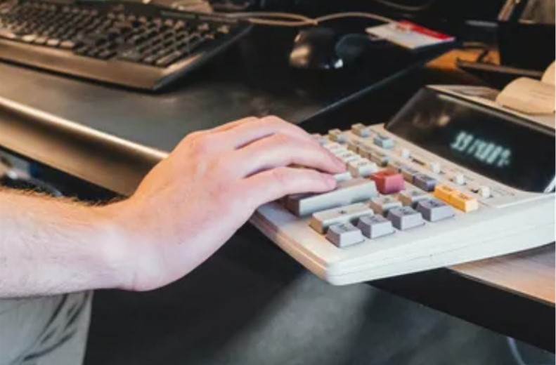 Photo of a hand at a ten key calculator on a desk.