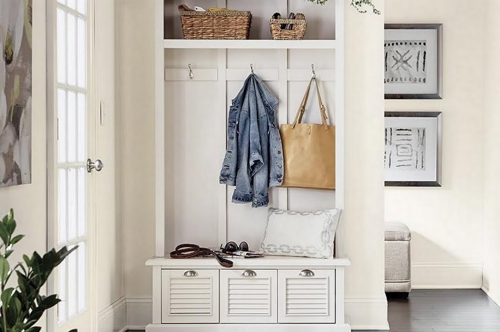 Photo of a decorated entryway with a hall tree housing baskets, a jacket, a purse, a leash, and a pillow. Art can be seen around the hall tree.