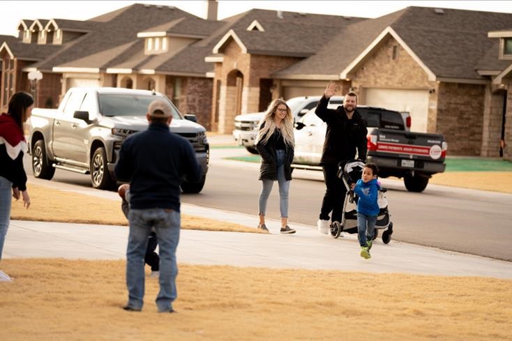 Photo of a husband and wife pushing a stroller down a community sidewalk waving to neighbors in their front yard. An HOA can help mitigate neighborhood disputes.