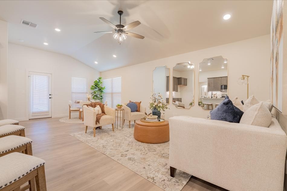 Bright and open living room with vaulted ceiling, ceiling fan, hardwood floors, and modern furnishings in a new Betenbough home