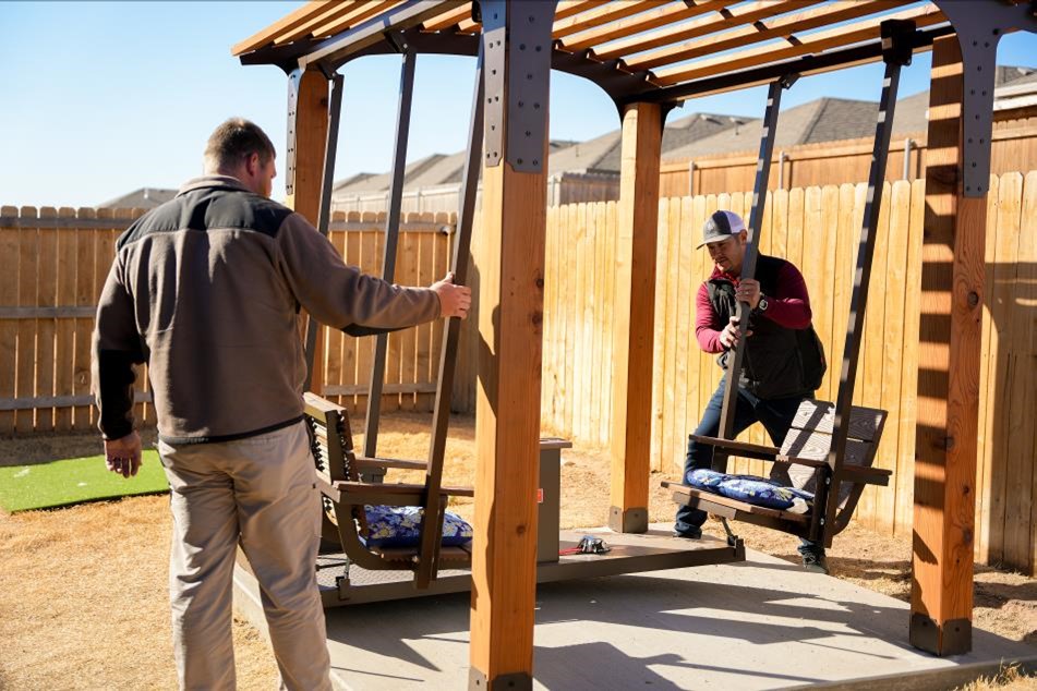 Photo of two men building a pergola with swings in the back yard of a Betenbough home.