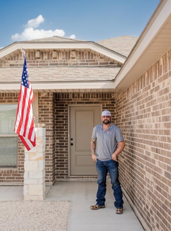 A man stands outside his Betenbough home with peace of mind because as a first-time home buyer, his monthly living costs will remain stable.