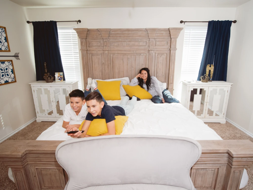 Photo of a mom and two sons relaxing on a big bed while they watch TV.