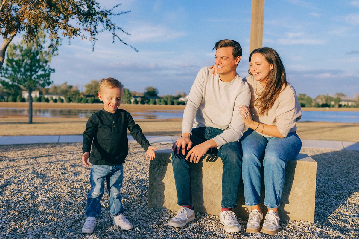 A young family with their toddler son sitting together outdoors in a Betenbough Homes community